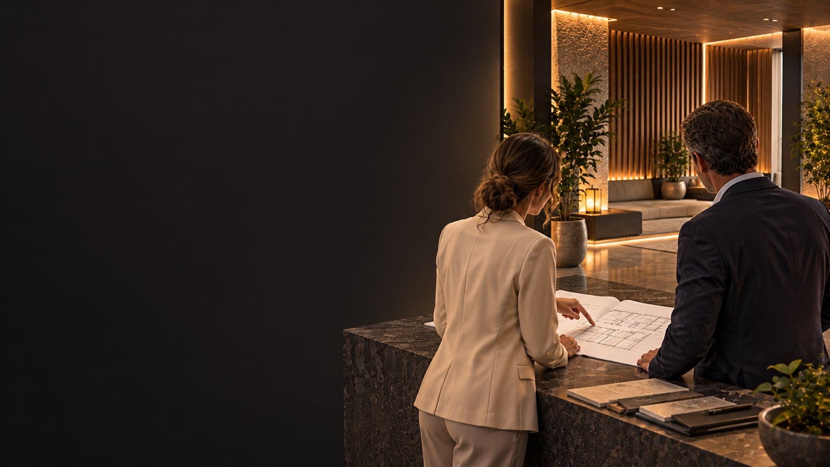 A woman and a man discuss plans spread out on a stone counter in a lobby